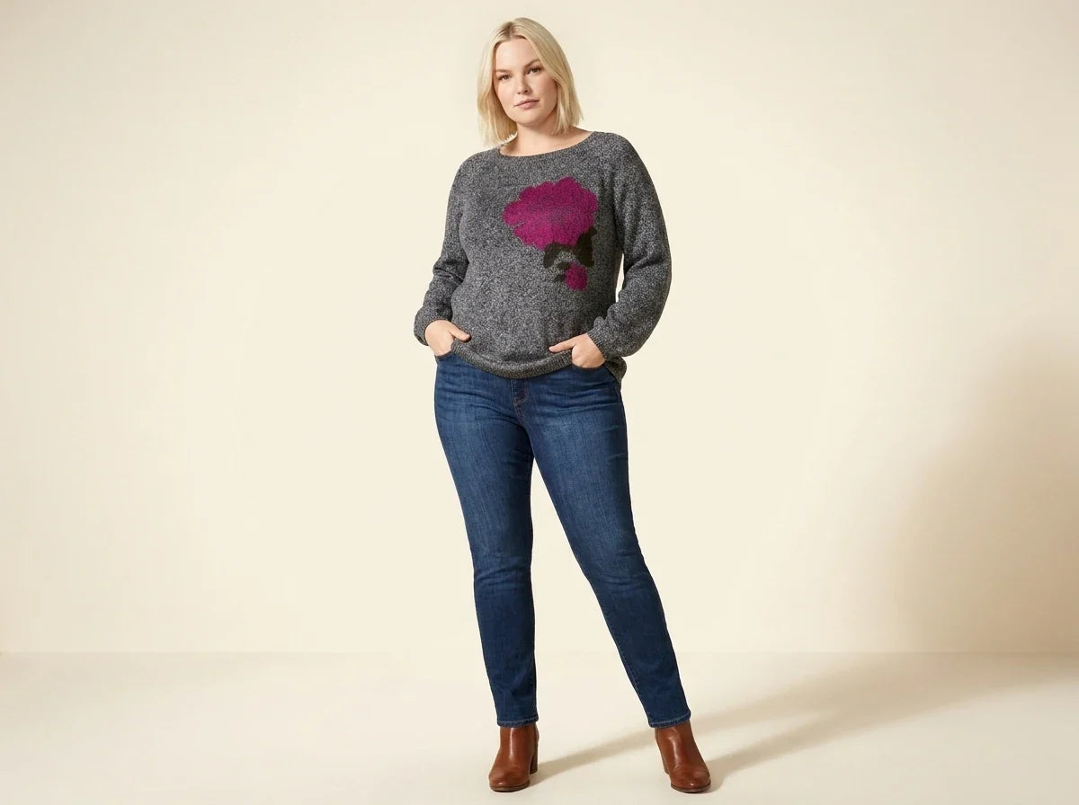 Blonde woman modeling a plus-size charcoal heather grey knit sweater with a magenta floral graphic, medium-wash skinny jeans, and brown leather ankle boots.