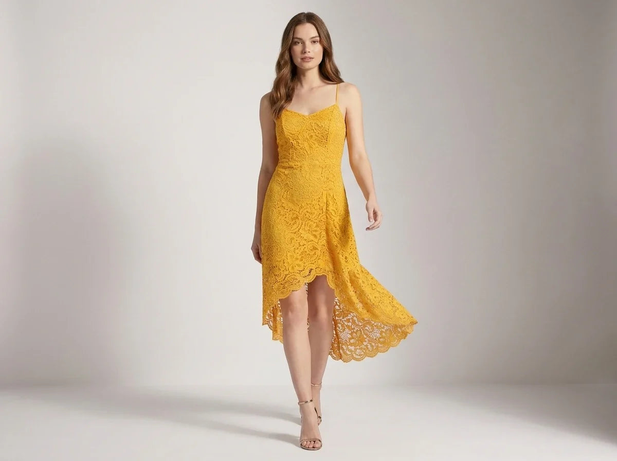 A woman modeling a bright yellow lace slip dress with spaghetti straps and a high-low hemline, standing against a neutral light gray studio backdrop.