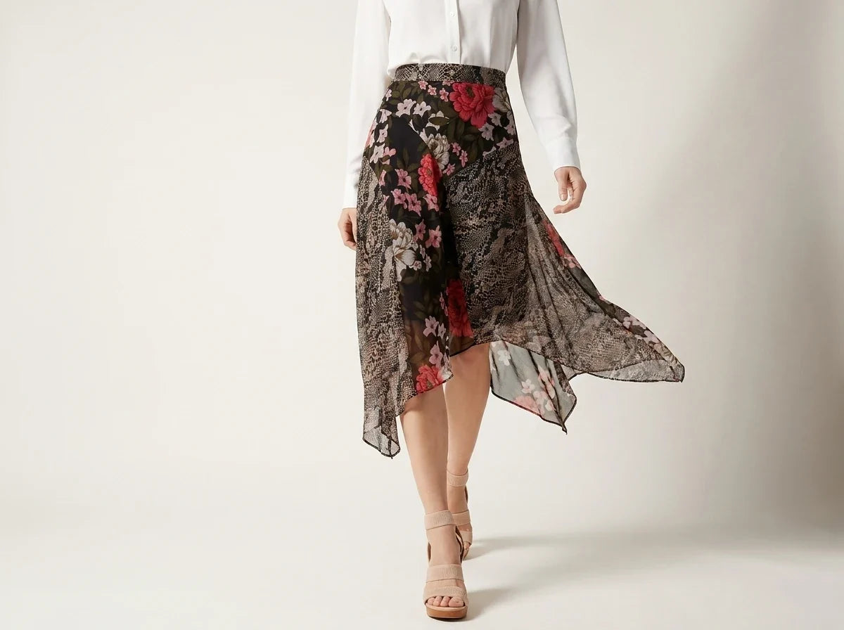 A model wearing a black high-waisted midi skirt with a red and pink floral lace overlay, paired with a white long-sleeve top and beige heeled sandals, set against a plain light gray studio background.