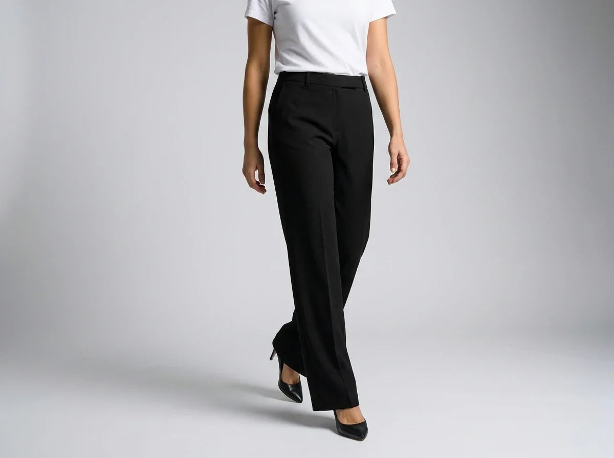 A model wearing black wide-leg trousers, styled with a white short-sleeve top and black pointed-toe heels, shown from the waist down against a light gray studio background.