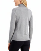 A woman shown from the back wearing a light gray ribbed mock neck sweater with button details on the cuffs, paired with black pants, against a plain white background.