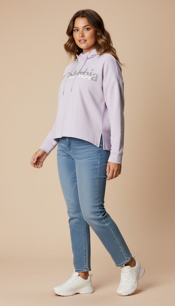 Woman wearing a light purple hoodie with text and blue jeans on a beige background