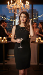 Woman in a black dress holding a cocktail at a formal event with a chandelier and city lights in the background.