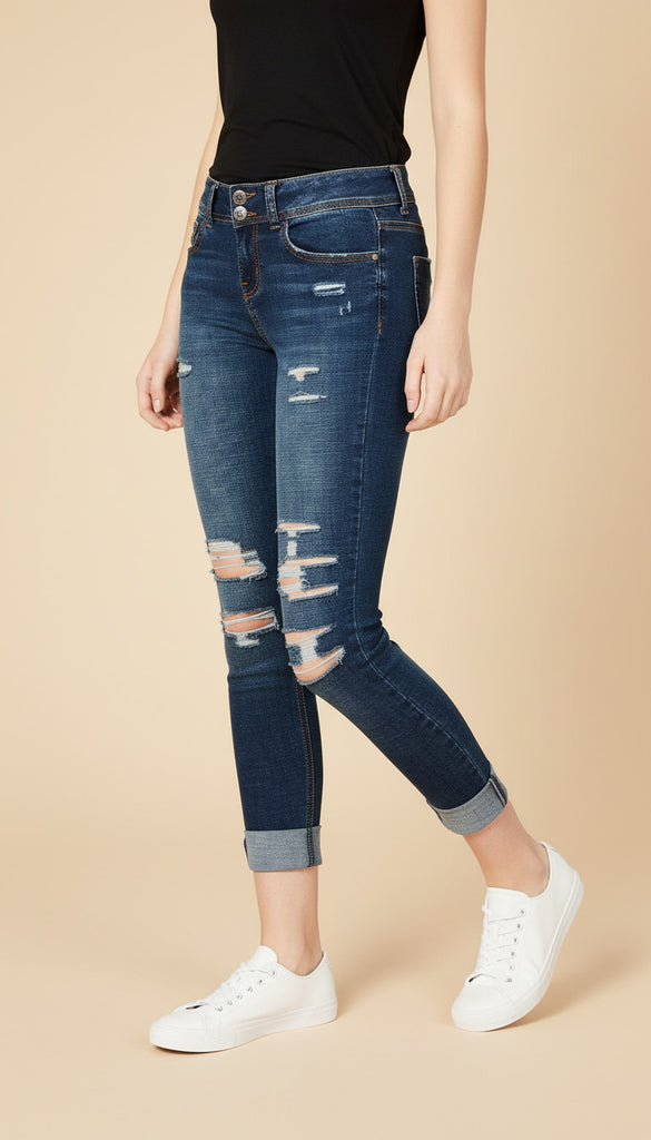 Person wearing distressed blue jeans and white sneakers on a beige background