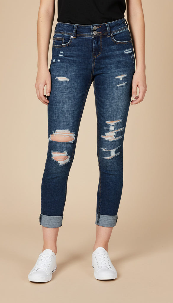 Person wearing distressed blue jeans and white sneakers on a beige background