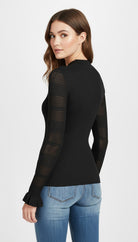 Woman wearing a black long-sleeve top with mesh panels and blue jeans on a white background
