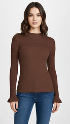 Woman wearing a brown ribbed long-sleeve top and blue jeans on a white background