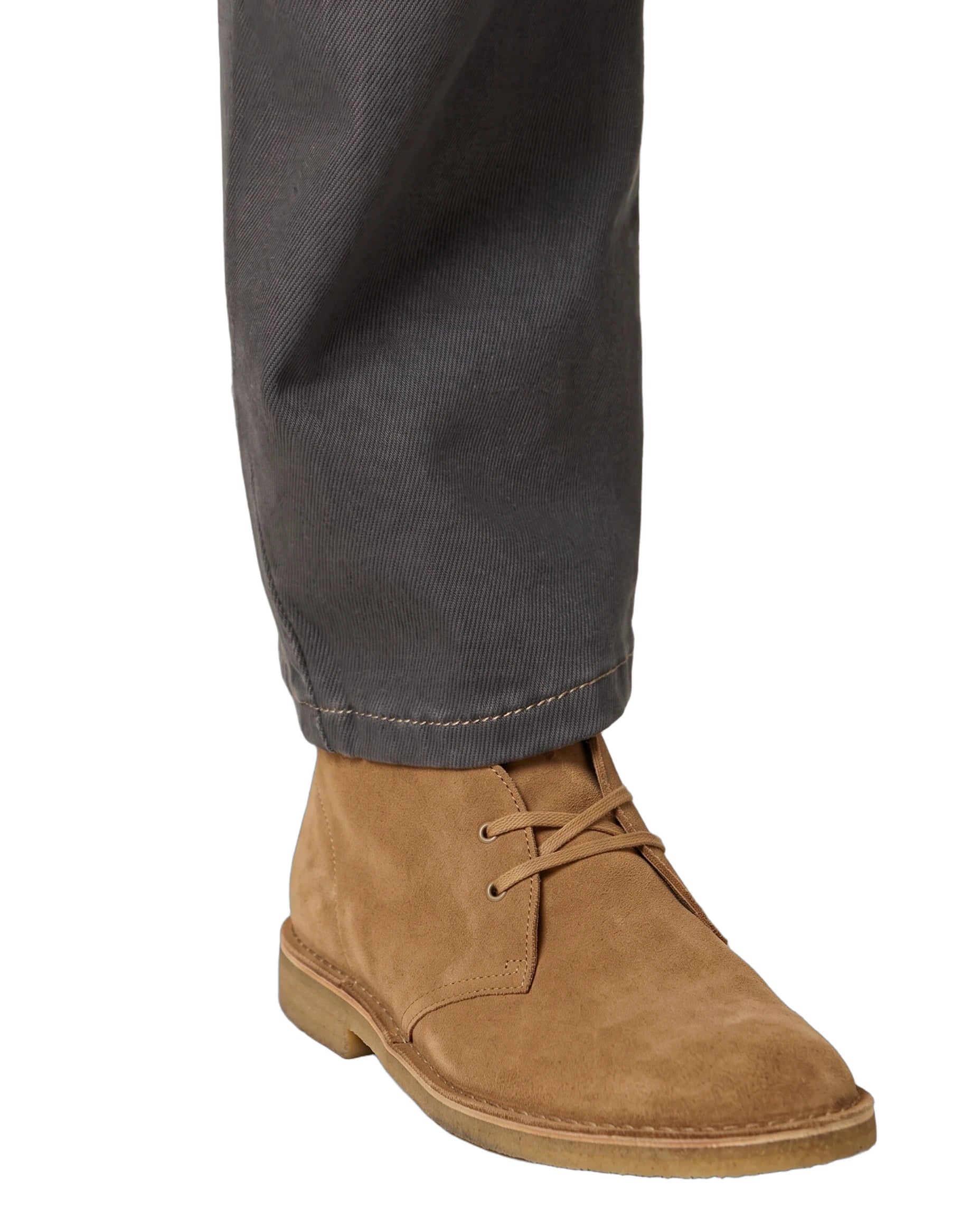 A close-up of a person's foot wearing a tan suede lace-up ankle boot with dark gray trousers, shown against a plain white background.