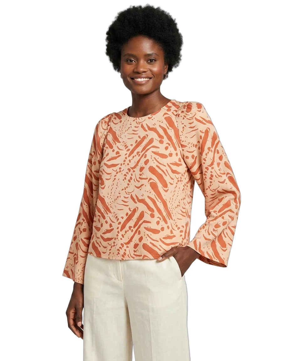 Woman wearing a patterned orange and beige top with white pants on a white background