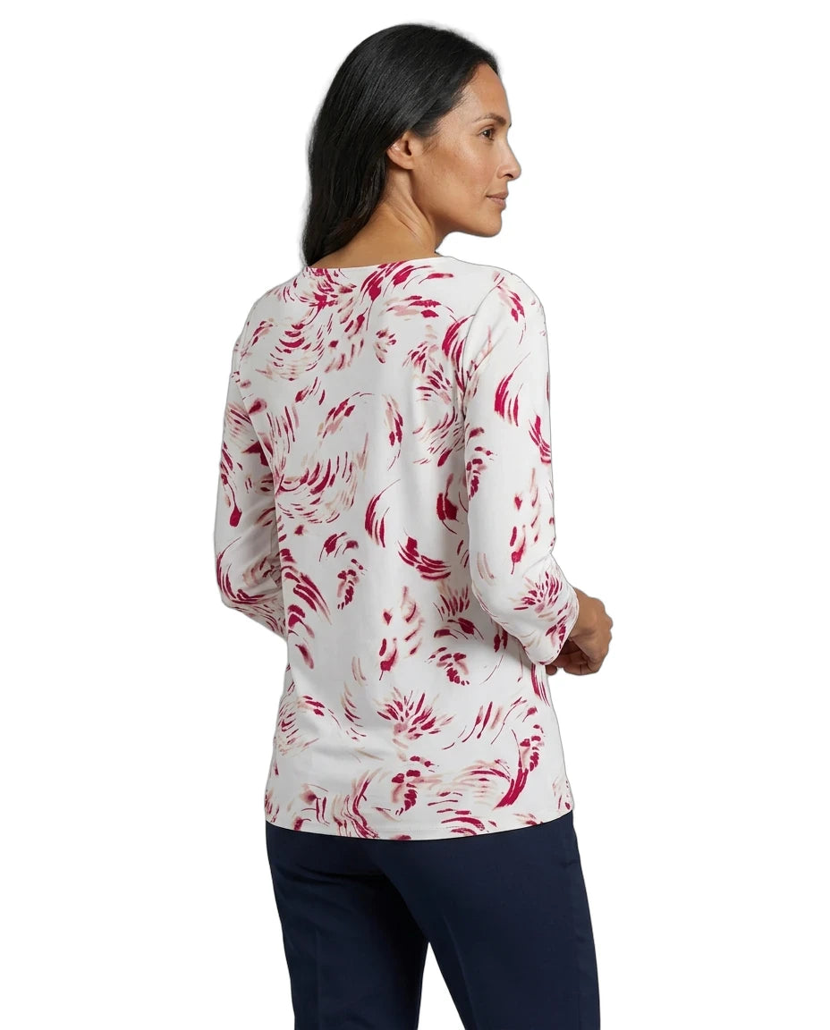A woman shown from the back wearing a white long-sleeve top with a pink abstract floral pattern, paired with dark navy pants, against a plain white background.