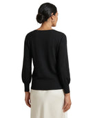 A woman shown from the back wearing a black long-sleeve knit top with balloon sleeves and a cream-colored skirt, against a plain white background.