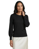 A woman modeling a black long-sleeve knit top with balloon sleeves, paired with a white skirt, against a plain white background.