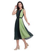 A woman modeling a sleeveless pleated midi dress with a color-blocked design in dark green and light green, featuring a black waistband and black side panels, paired with beige high heels against a white background.