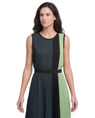 A woman modeling a sleeveless pleated dress with vertical color-blocked panels in dark charcoal gray, black, and light sage green, featuring a matching waistband.
