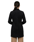 A woman viewed from the back wearing a black long-sleeve blazer or coat over tan pants, photographed against a plain white studio background.