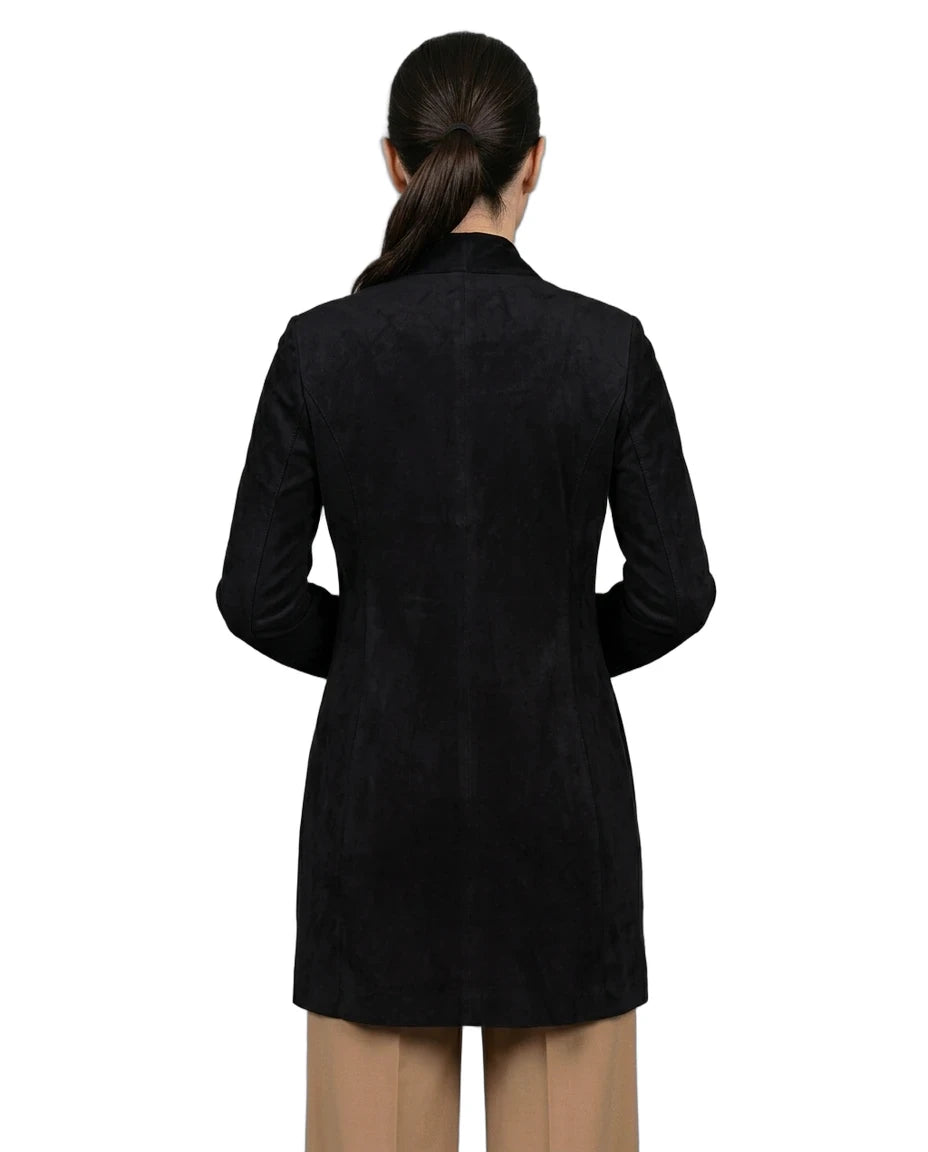 A woman viewed from the back wearing a black long-sleeve blazer or coat over tan pants, photographed against a plain white studio background.