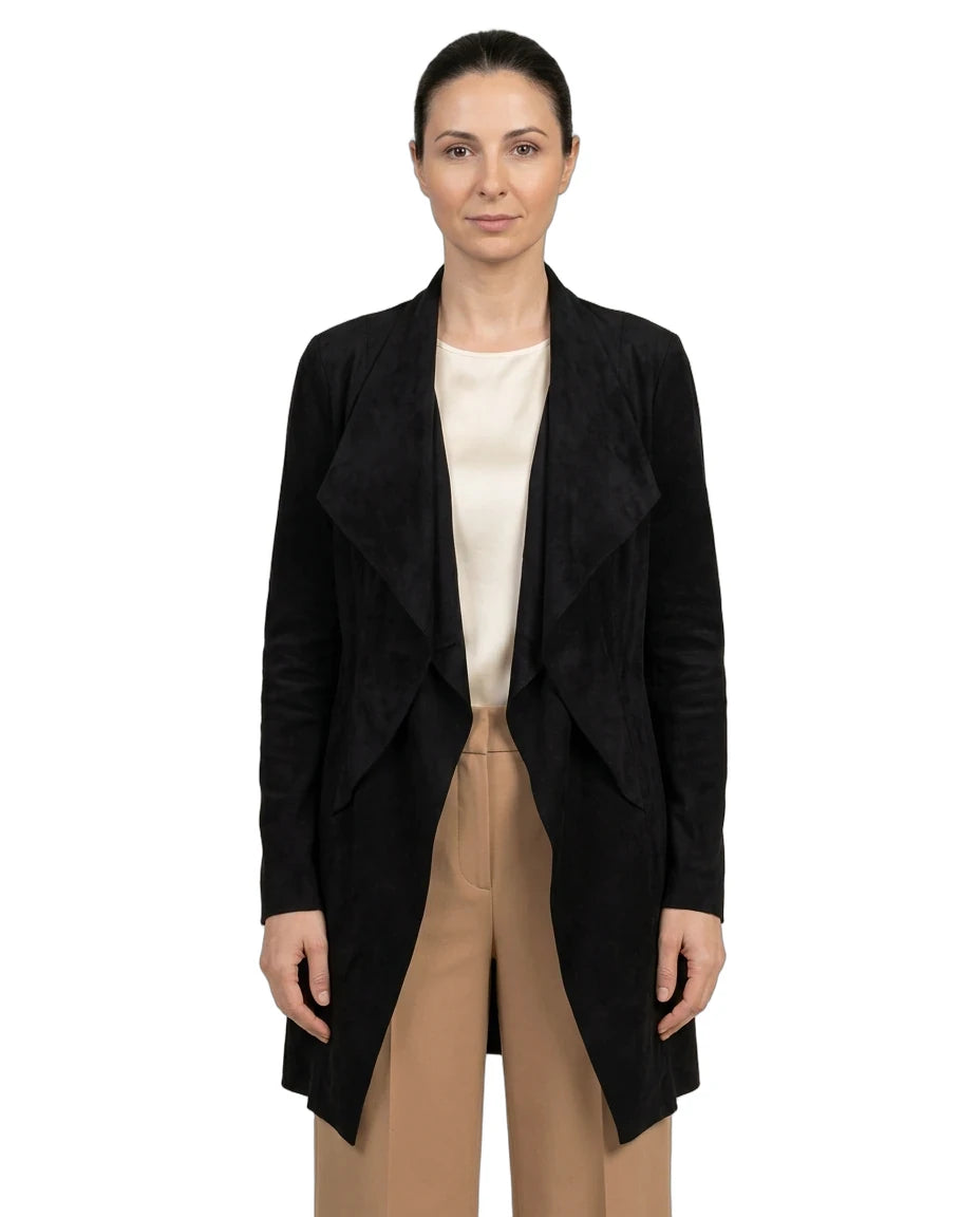 A woman modeling a black open-front wrap-style coat over a cream top and beige trousers, photographed against a plain white studio background.
