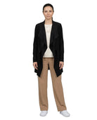 A woman modeling a black open-front draped cardigan over a cream top and beige wide-leg trousers, paired with white sneakers, against a plain white background.