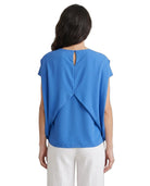 Woman wearing a blue top with a cut-out back design on a white background