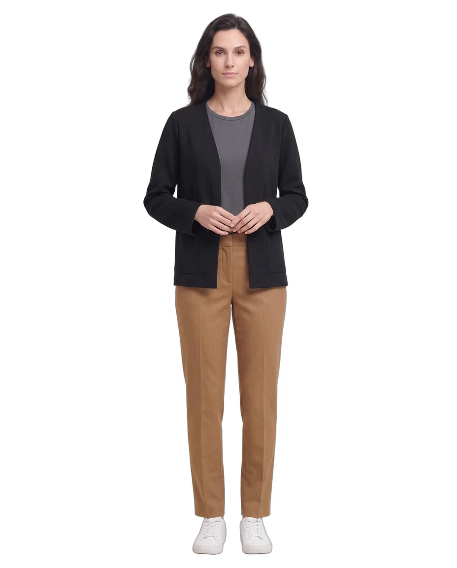 A woman stands against a plain white background wearing a black open-front cardigan over a gray top, tan pants, and white sneakers.