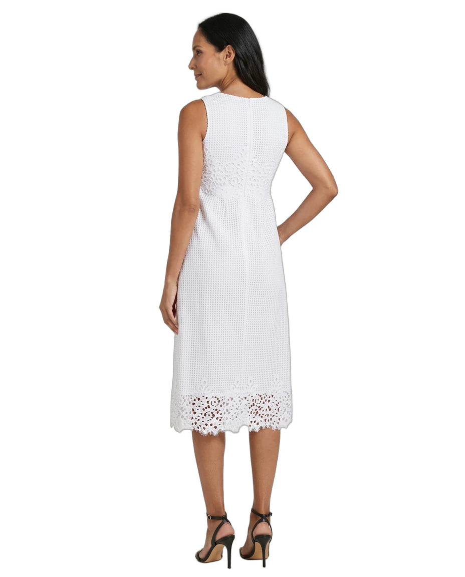 A woman shown from the back wearing a sleeveless white midi dress with a textured woven pattern and eyelet lace trim at the hem, paired with black high-heeled sandals against a plain white background.