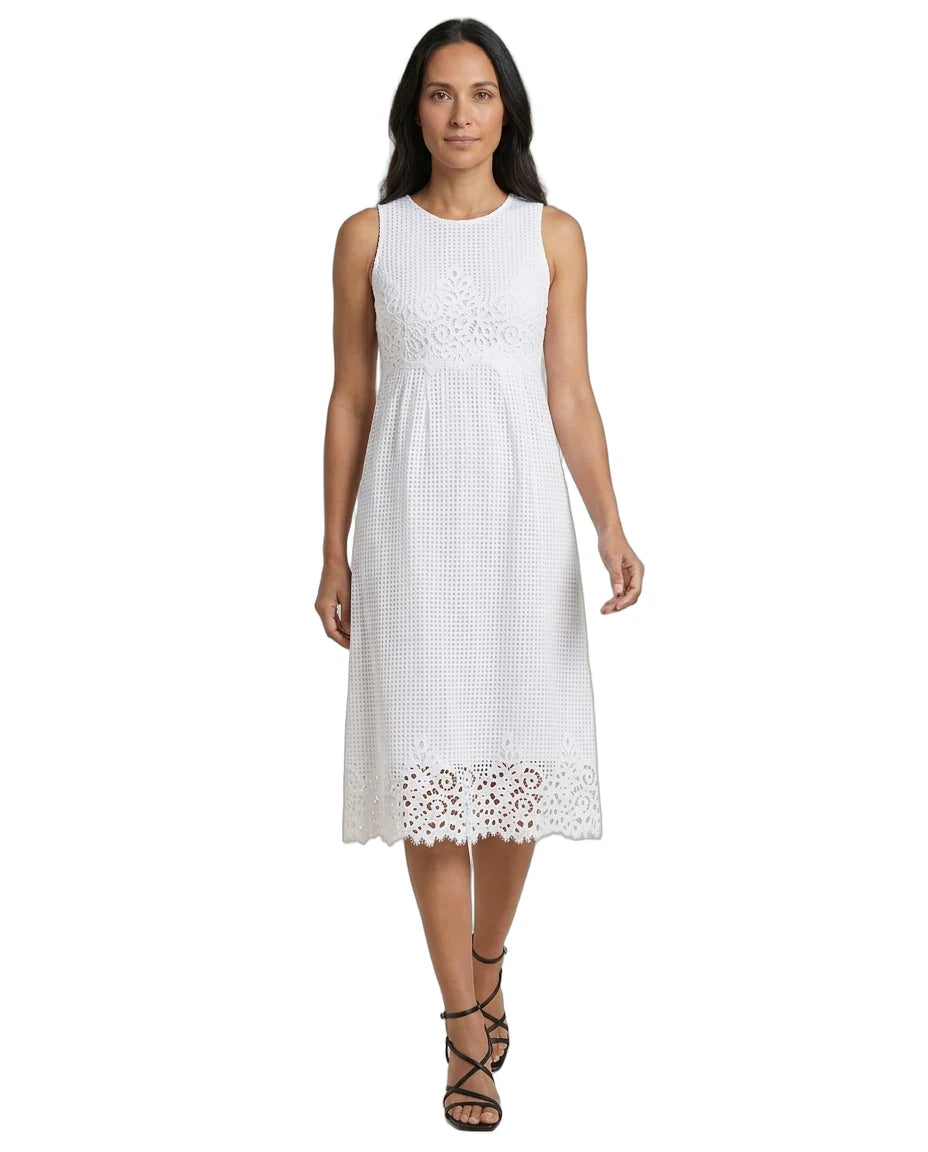 A woman modeling a sleeveless white midi dress with a textured eyelet pattern and lace trim at the hem, paired with black strappy high-heeled sandals against a plain white background.