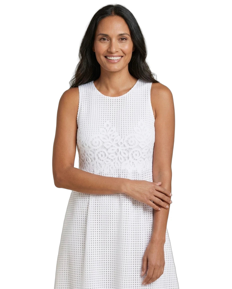 A woman modeling a sleeveless white eyelet dress with a textured, openwork pattern against a solid white background.