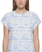 A woman wearing a short-sleeve crewneck top with a blue and white abstract horizontal stripe pattern, shown against a plain white background.