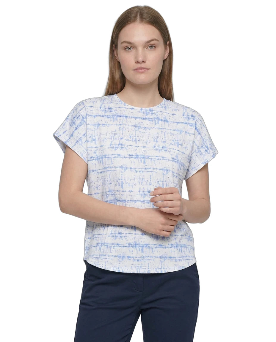 A woman modeling a short-sleeve crewneck top with a blue and white abstract textured pattern, paired with navy pants, against a plain white background.
