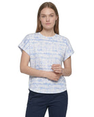 A woman modeling a short-sleeve crewneck top with a blue and white abstract textured pattern, paired with navy pants, against a plain white background.
