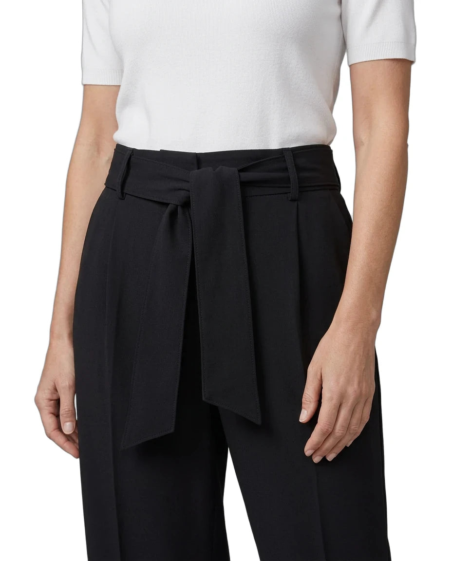 A model wearing black wide-leg trousers with a matching self-tie belt, paired with a white short-sleeve top, shown from the chest down on a white studio background.