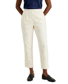 A model wearing off-white cropped trousers with an eyelet cutout pattern, paired with a navy top and black loafers, shown from the waist down on a white background.