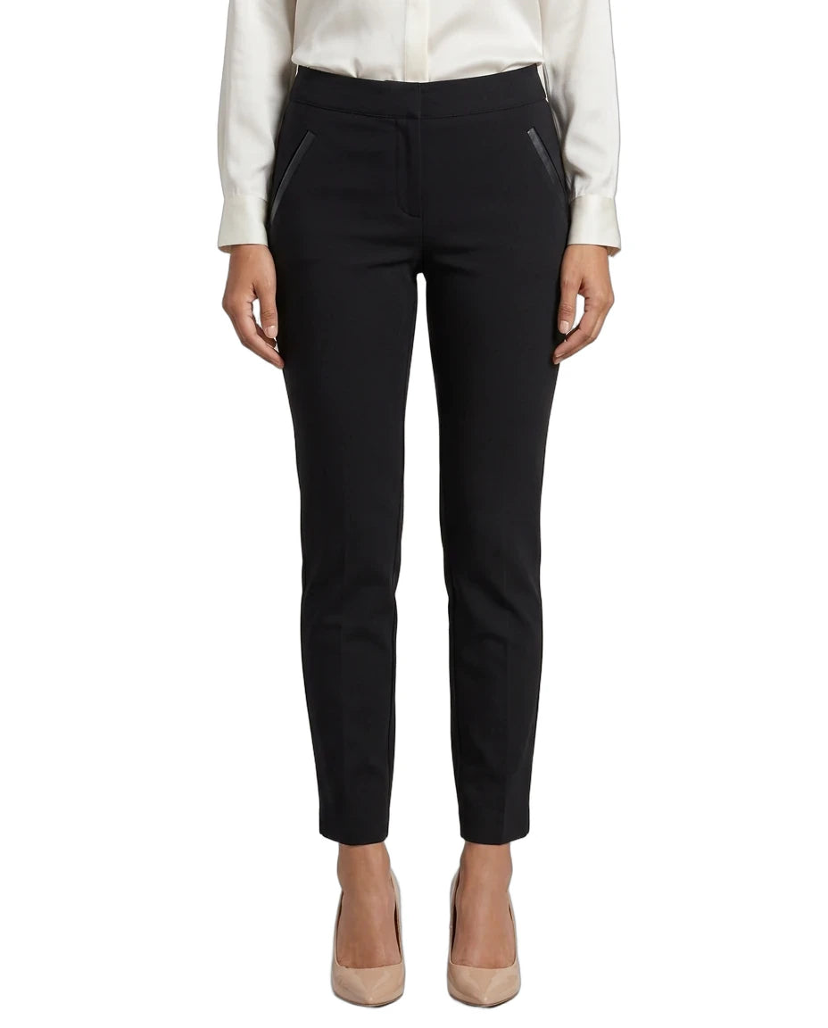 A model from the waist down wearing slim black trousers with diagonal zippered pockets, styled with a white blouse and beige heels against a plain white background.