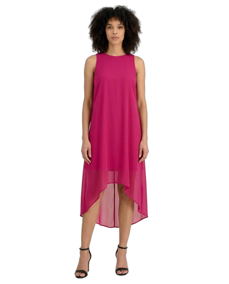 A woman modeling a sleeveless high-low midi dress in a vibrant magenta pink, paired with black strappy high-heeled sandals, against a plain white background.