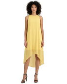 A woman modeling a sleeveless high-low midi dress in a soft pastel yellow, paired with black strappy high-heeled sandals against a plain white background.
