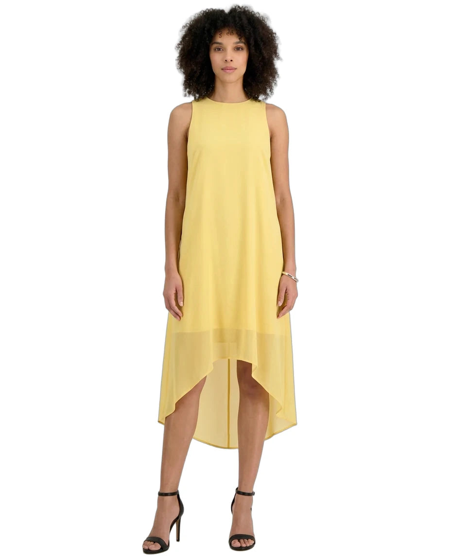 A woman modeling a sleeveless high-low midi dress in a soft pastel yellow, paired with black strappy high-heeled sandals against a plain white background.