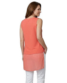 Woman wearing a coral sleeveless top and white pants on a white background