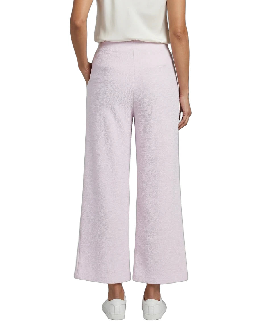 A model shown from the back wearing light pink wide-leg cropped pants, a cream top, and white sneakers against a plain white background.