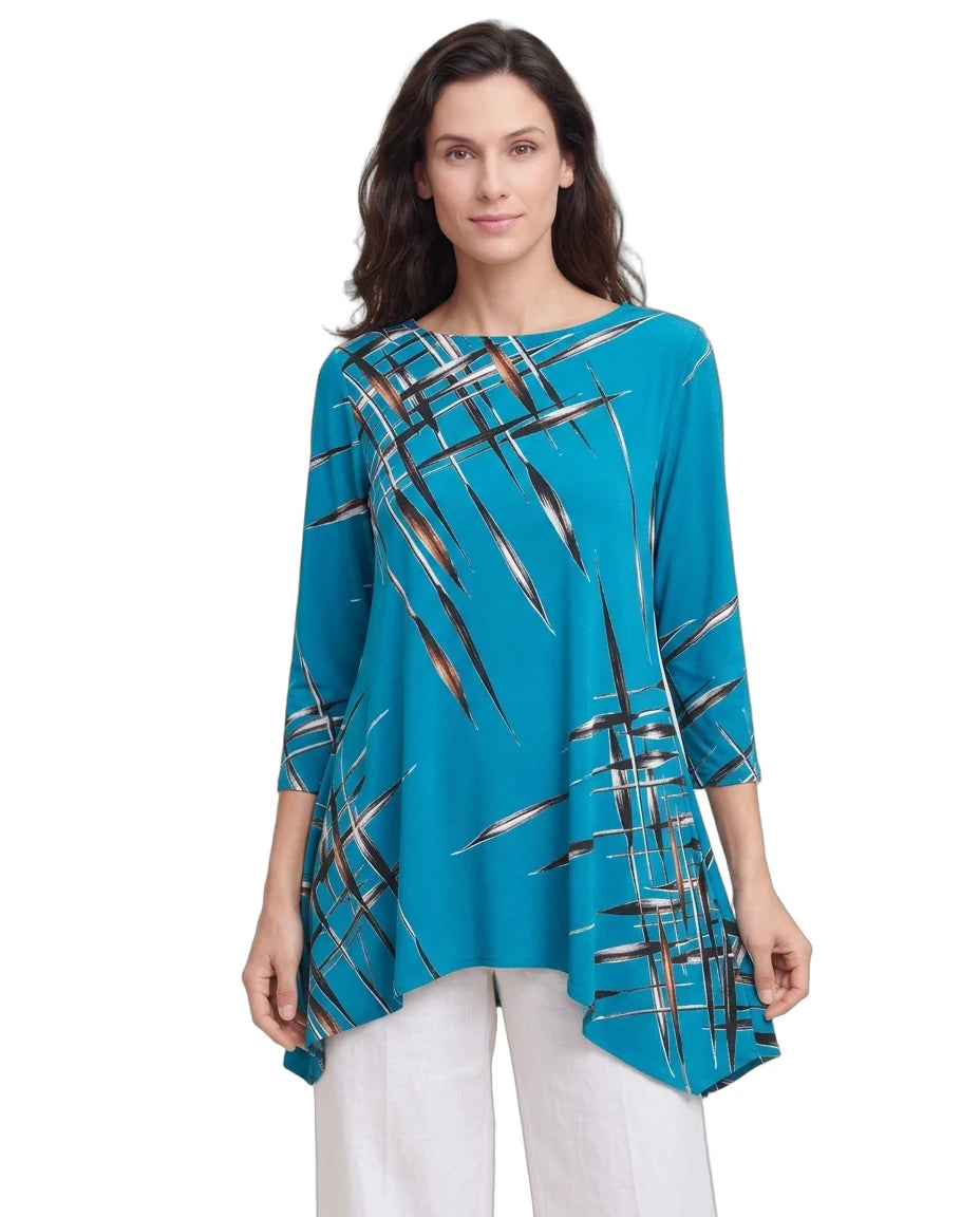 A woman modeling a turquoise blue three-quarter sleeve tunic top with a black, white, and brown abstract brushstroke pattern, paired with white pants, against a plain white background.