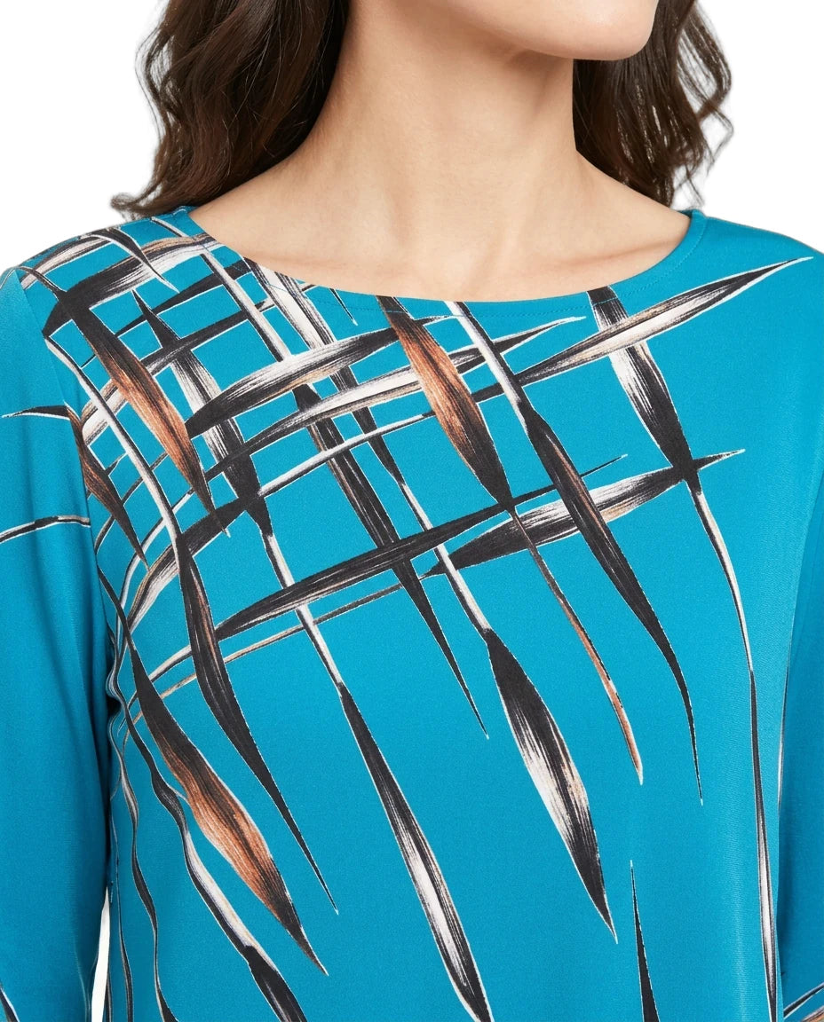 A close-up of a model wearing a bright turquoise blue top with a black, white, and brown abstract leaf-like pattern across the chest.