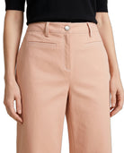 A close-up of a model wearing high-waisted peach-colored wide-leg trousers with belt loops, a silver button, and welt pockets, paired with a black top.