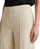 Close-up of a person wearing high-waisted, wide-leg trousers in a light beige linen-like fabric, paired with a black top against a plain white background.