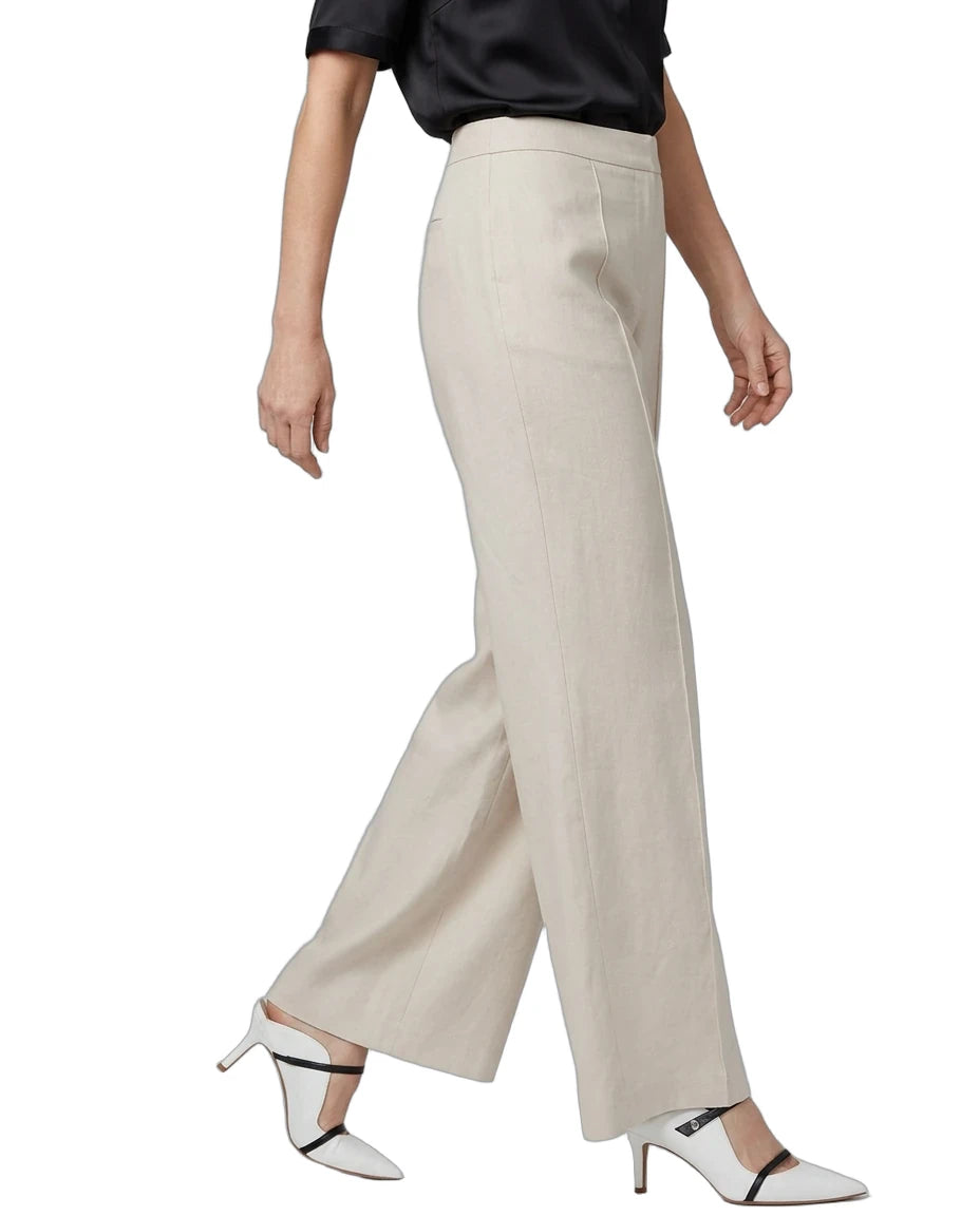 A model wearing a pair of high-waisted, wide-leg trousers in a light beige linen-like fabric, styled with a black short-sleeve top and white heeled sandals with black straps, against a plain white background.