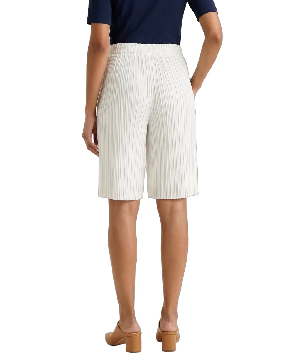 A model shown from the back wearing pleated white shorts, a navy blue top, and tan block-heel mules against a plain white background.