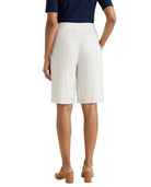 A model shown from the back wearing pleated white shorts, a navy blue top, and tan block-heel mules against a plain white background.