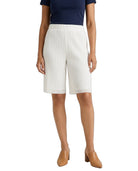 A model wearing white pleated knee-length shorts, a navy blue top, and tan mule heels, shown from the waist down against a plain white background.