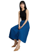A woman wearing a sleeveless black top and a pleated royal blue midi skirt, paired with tan pointed-toe heels, posed against a solid white background.