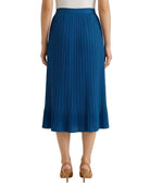 A model from the back wearing a vibrant blue pleated midi skirt, paired with a white top and tan high-heeled sandals, set against a plain white background.