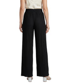 Black pleated wide-leg trousers shown from the back on a model, paired with a cream top and metallic silver heels, against a plain white background.