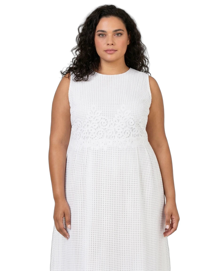 A woman modeling a sleeveless white dress with a textured eyelet pattern and a decorative embroidered band at the waist, shot against a plain white background.